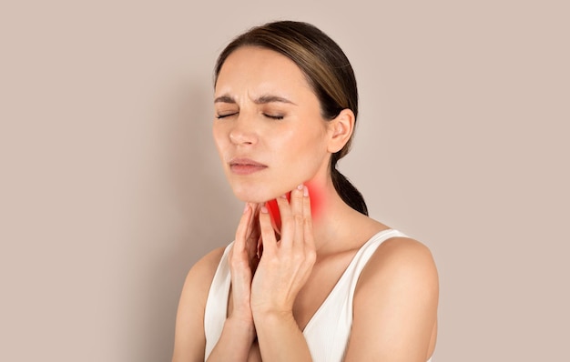Kobieta cierpiąca na ból gardła dotykająca szyi beżowym tle