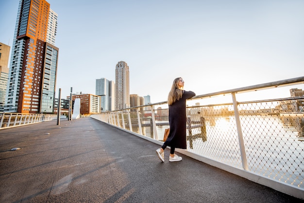 Kobieta ciesząca się nowoczesnym widokiem na miasto stojąca na moście rano w mieście Roterdam