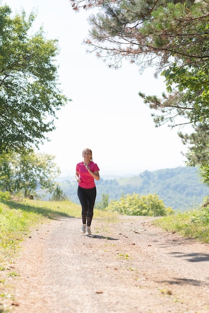 kobieta ciesząca się zdrowym stylem życia podczas joggingu na wiejskiej drodze przez piękny słoneczny las, koncepcja ćwiczeń i fitness