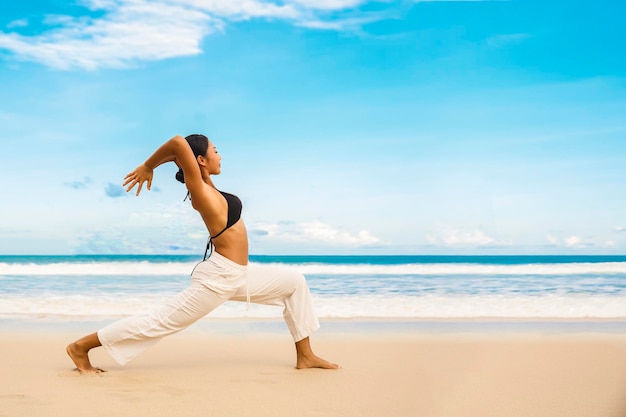 Kobieta ćwicząca jogę nad brzegiem morza w tropikalnej plażySportowa dama stojąca na plaży wykonuje ćwiczenia jogi