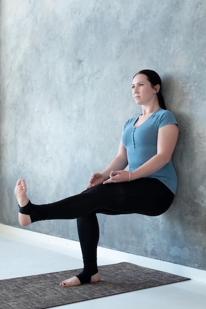 Kobieta ćwicząca jogę stojąca w pozie Utkatasana Chair w pobliżu ściany, podnosząca nogę do góry