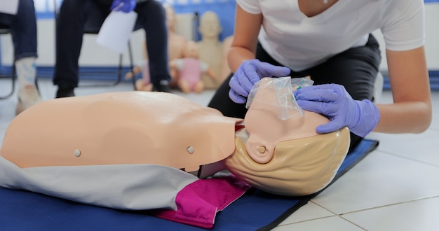 Kobieta ćwicząca resuscytację krążeniowo-oddechową na manekinie w klasie pierwszej pomocy.