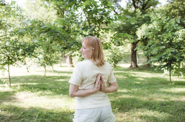 Kobieta ćwiczy jogę w parku na świeżym powietrzu z rękami skrzyżowanymi za plecami zdrowy tryb życia