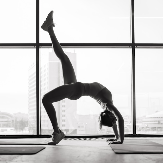 Kobieta ćwiczy zaawansowaną jogę na macie przed dużym oknem