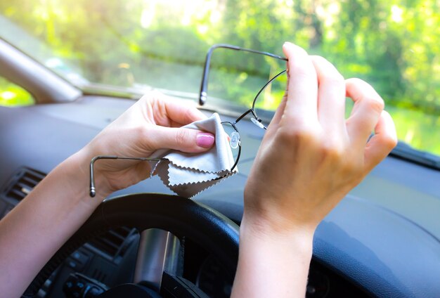 Kobieta czyści okulary za kierownicą. Dziewczyna prowadząca samochód.