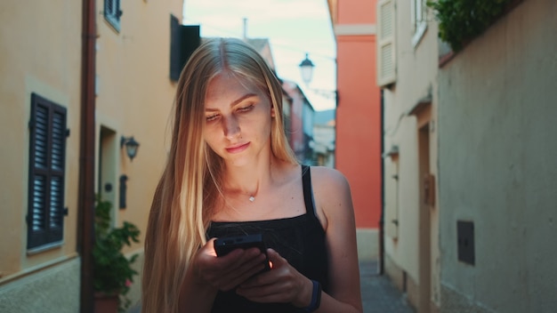 Kobieta czyta coś na smartfonie podczas spaceru ulicą. Była szczęśliwa i uśmiechnięta. Czas letni.