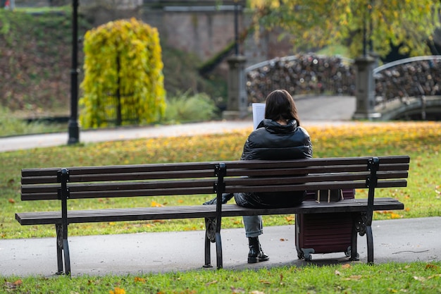 Kobieta czyta książkę i siedzi na ławce w jesiennym parku Jesienny nastrój czasu wolnego Widok z tyłu