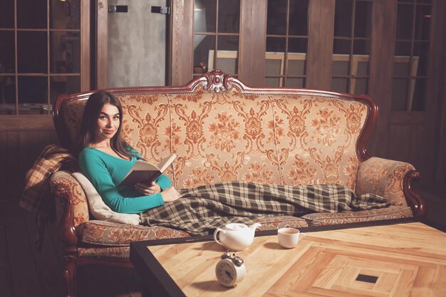 Kobieta czyta książkę na pięknej kanapie w kwadratową kratę przy stole