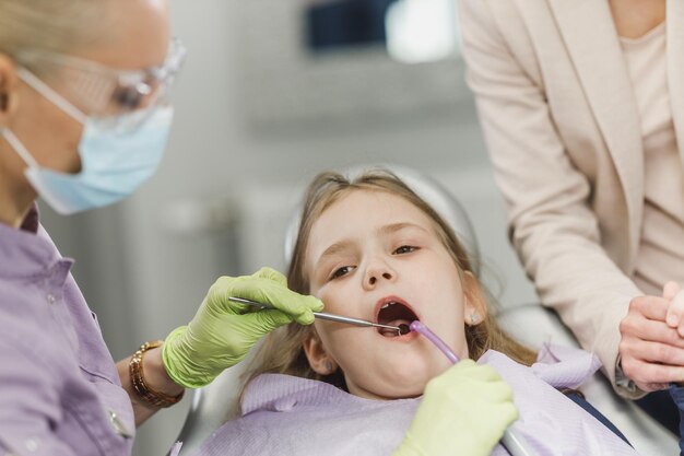 Kobieta dentysta badając słodkie dziewczynki zęby podczas zabiegu stomatologicznego w gabinecie dentystycznym.