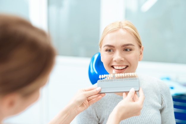 Kobieta dentysta określa kolor zębów pacjenta.