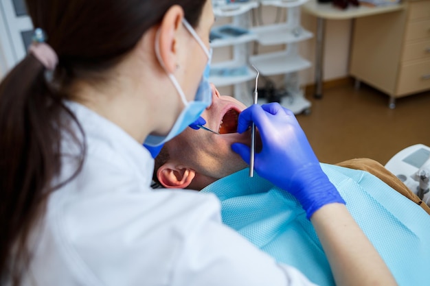 Kobieta dentysta podczas leczenia pacjenta. Lekarz dokonuje leczenia stomatologicznego na zębach osoby siedzącej na fotelu dentystycznym. Selektywne skupienie.