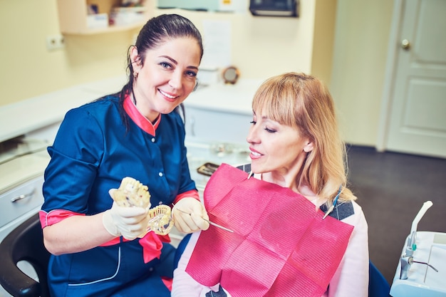 Kobieta dentysta pokazująca sztuczną szczękę pacjenta w gabinecie stomatologicznym
