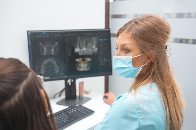 Kobieta dentysta rozmawia ze swoim pacjentem, pokazując zdjęcie rentgenowskie na komputerze