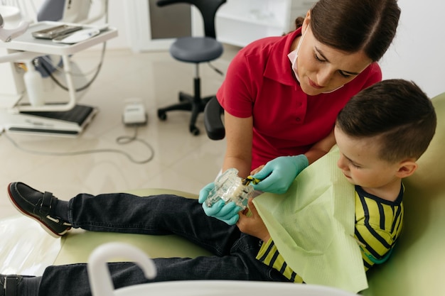 Kobieta dentysta uczy chłopca, jak myć zęby na fotelu dentystycznym