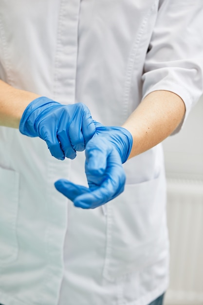 Kobieta dentysta zakłada rękawiczki na tle sprzętu dentystycznego w gabinecie stomatologicznym
