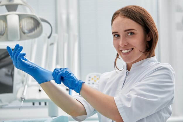 Kobieta dentysta zakłada rękawiczki w gabinecie stomatologicznym. Koncepcja szczęśliwy pacjenta i dentysty.