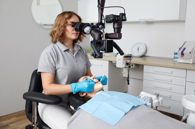 Zdjęcie kobieta dentystka z narzędziami dentystycznymi i mikroskopem lecząca zęby pacjenta w klinice stomatologicznej