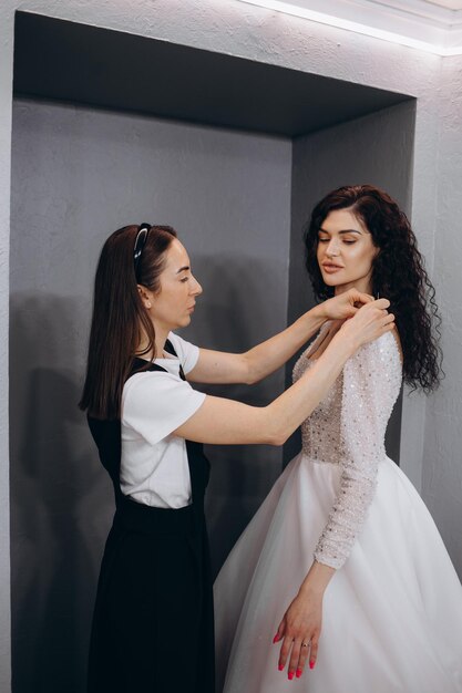 Kobieta dopasowująca się do sukni ślubnej w studio projektantów mody Panna młoda ubrana w suknię ślubną z projektantką dokonującą ostatecznych poprawek w sukience