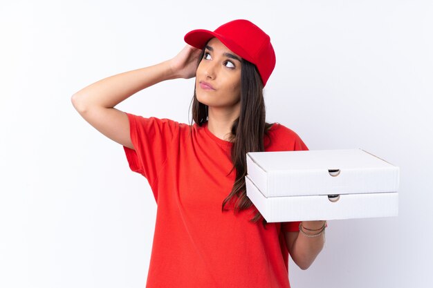 Kobieta dostawy pizzy trzyma pizzę na pojedyncze białe ściany, mając wątpliwości i mylić wyraz twarzy