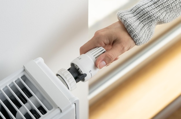 Kobieta dostosowuje termostat grzejnikowy do maksymalnej temperatury w pomieszczeniu