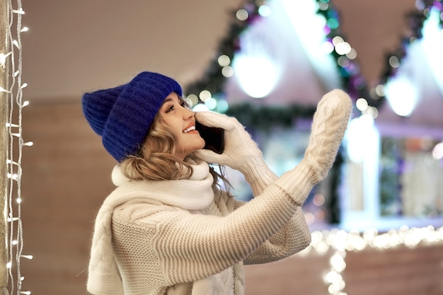 Kobieta dzwoniąc pogratulować Bożego Narodzenia lub Nowego Roku. Kobieta ze smartfonem na świątecznych targach.