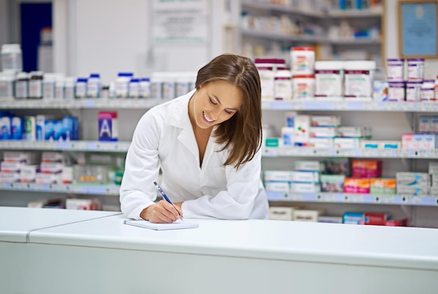 Kobieta farmaceutka i uśmiech na liczniku z pisaniem recept i planowaniem w aptece Specjalistka chemik i notatnik z długopisem do sprawozdania z informacji medycznych i zarządzania zapasami