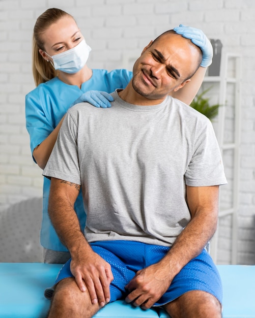 Zdjęcie kobieta fizjoterapeuty z maską medyczną sprawdzającą ból szyi mężczyzny
