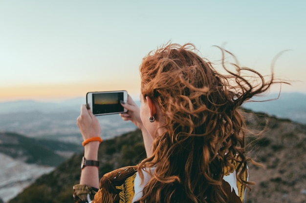 Kobieta fotografująca telefonem komórkowym na tle nieba