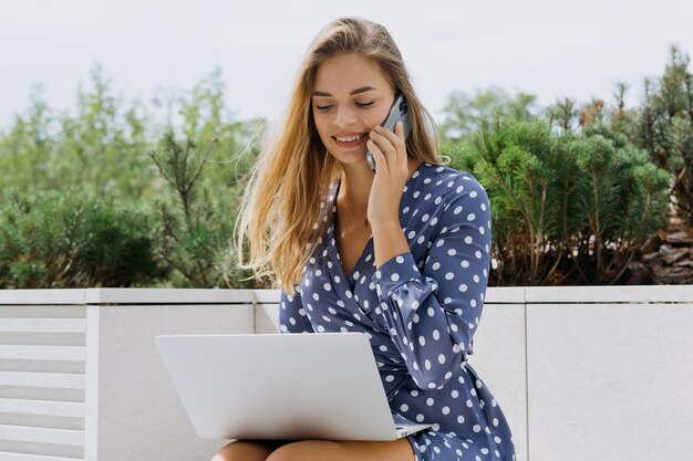 Kobieta freelancer Młoda uśmiechnięta kobieta rozmawia przez telefon podczas pracy na laptopie na zewnątrz