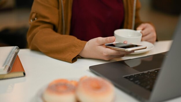 Zdjęcie kobieta freelancer zdalna pracująca w przestrzeni coworkingowej kawiarni przy użyciu smartfona i laptopa