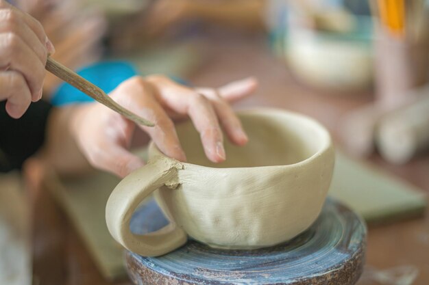 Kobieta garncarz pracuje na kole garncarskim wyrabia ceramiczny garnek z gliny w warsztacie garncarskim koncepcja sztuki Skupienie ręki młoda kobieta przyczepia glinianą część produktu do przyszłego wyrobu ceramicznego Warsztat garncarski