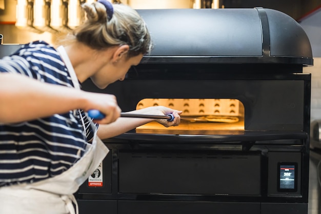 Kobieta gotuje pizzę w piecu elektrycznym, pizza maker w piekarni