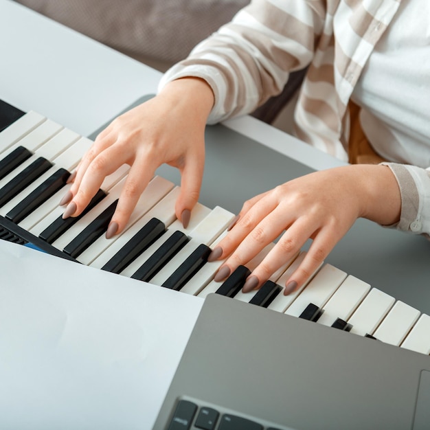 Kobieta gra na pianinie nagrywa muzykę na syntezatorze za pomocą notatek laptop kobiece ręce muzyk pianista imp...