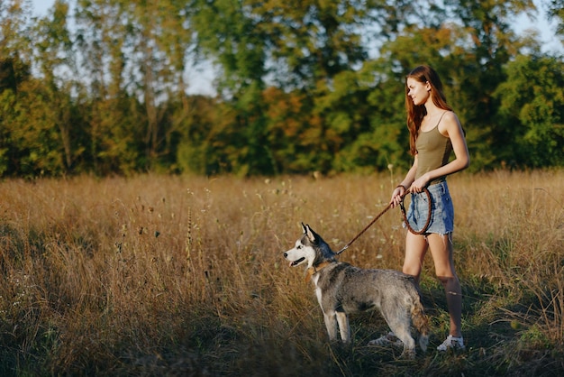 Kobieta i jej pies husky szczęśliwie chodzą i biegają po trawie na polu uśmiech z zębami o zachodzie słońca spacer ze zwierzakiem podróż z przyjacielem psem szczęście styl życia