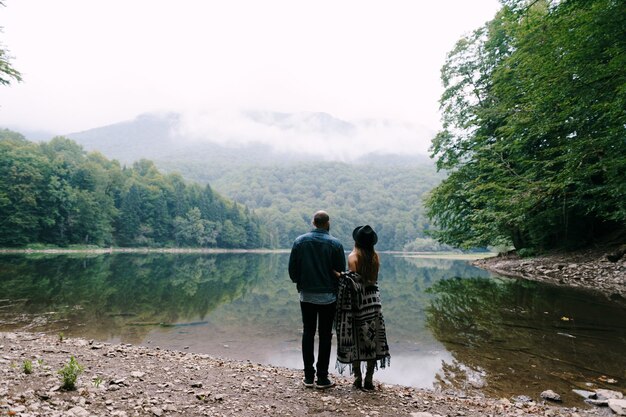 Kobieta i mężczyzna stoją nad jeziorem w parku i patrzą na góry z tyłu