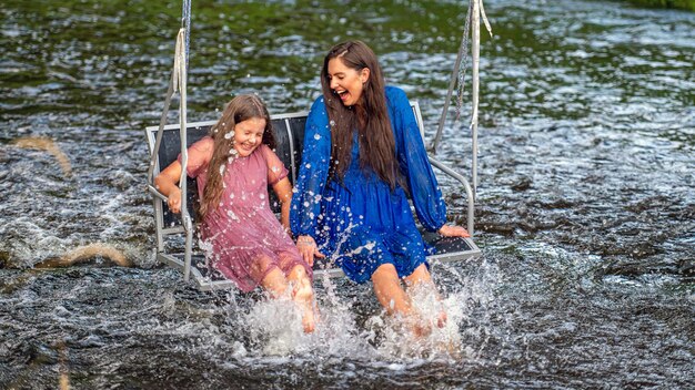 Kobieta i młoda dziewczyna huśtają się po rwącej rzece, śmiejąc się i chlapiąc wodą