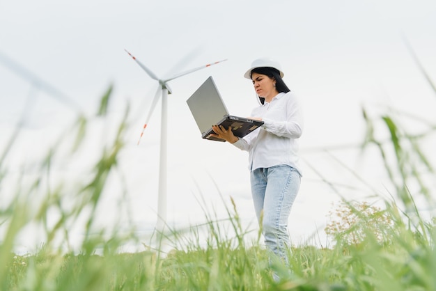 Kobieta inżynier w kasku na farmie turbin wiatrowych pracująca na laptopie
