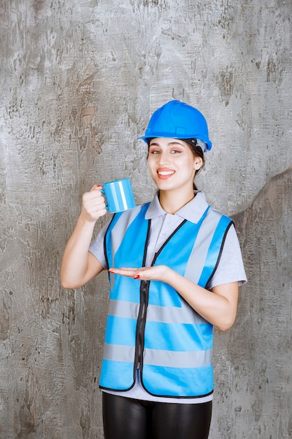 Kobieta inżynier w niebieskim mundurze i kasku, trzymając kubek z niebieską herbatą.