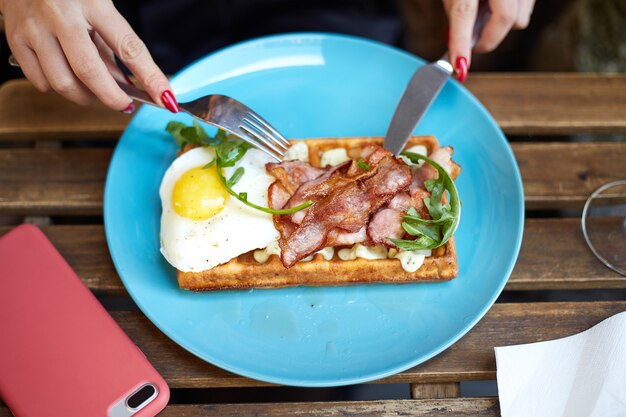 Kobieta je belgijskie gofry z bekonem, jajkiem i rukolą