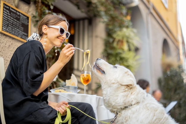 Kobieta je makaron ze swoim uroczym białym psem w restauracji