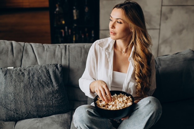 Kobieta je popcorn w domu na kanapie i ogląda film