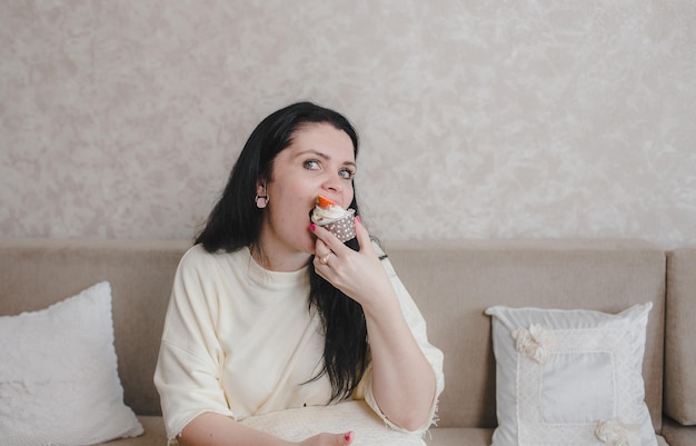 Kobieta je pyszną truskawkową babeczkę siedząc w domu na kanapie. domowy deser baw się dobrze