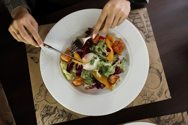 Kobieta Je Sałatkę Ze świeżych Warzyw Z Liśćmi Zielonej Sałaty I świeżej żółtej Papryki Z Kawałkami Ryb I Jajkiem W Koszulce W Restauracji. Widok Z Góry Z Bliska. Zdrowe śniadanie