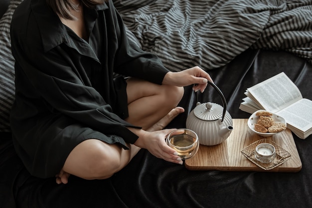 Kobieta je śniadanie z herbatą i ciasteczkami, leżąc w łóżku w dzień wolny.