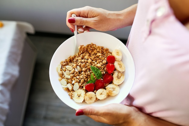 Kobieta je zdrową miskę śniadaniową, trzymaj w ręku muesli, nasiona, świeża truskawka, banan, widok z góry, miejsce. Czyste odżywianie, detoksykacja, dieta, koncepcja żywności wegetariańskiej