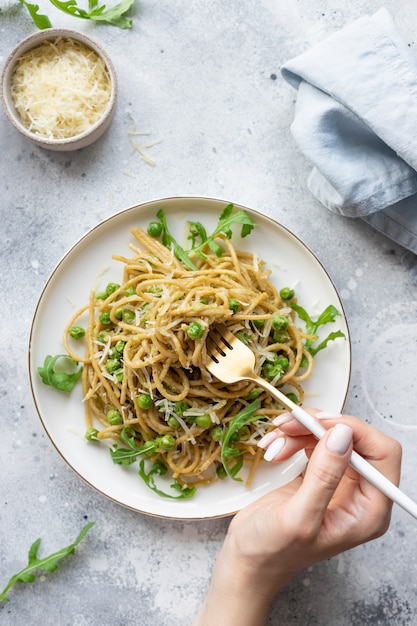 Kobieta jedzenie wegańskiego makaronu spaghetti z zielonym groszkiem i awokado