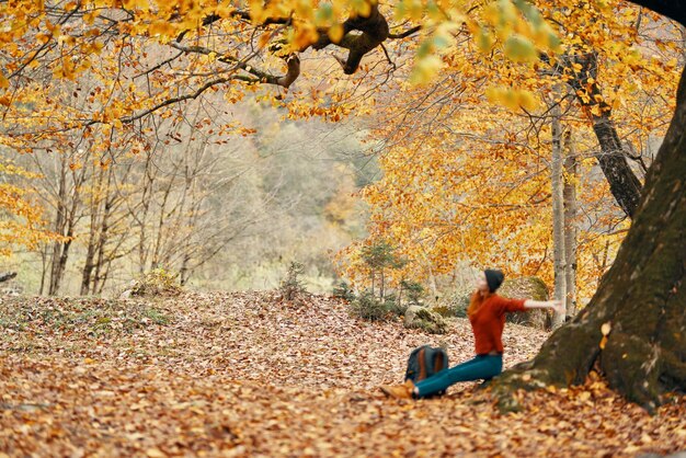 Kobieta jesienią w parku w pobliżu dużego drzewa i w plecaku na ziemi wysokiej jakości zdjęcie