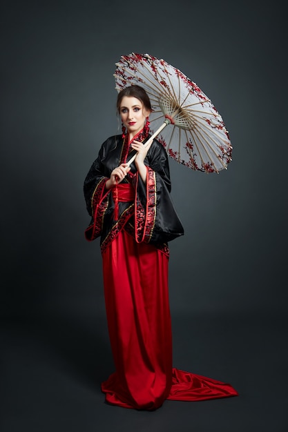 Kobieta jest ubrana w czerwone chińskie japońskie stroje ludowe. Latająca tkanina, piękny parasol i wachlarz w japońskim stylu chińskim, długie kolczyki w uszach. Dziewczyna pozuje na ciemnym tle