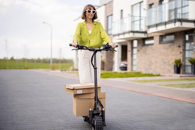 Kobieta jeżdżąca skuterem elektrycznym z kartonowymi paczkami
