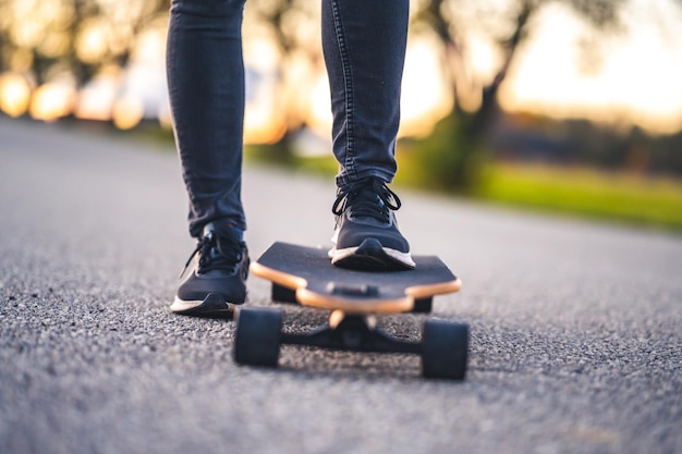 Kobieta jeździ po prostej drodze na longboardzie o zachodzie słońca Łyżwiarka w stroju casualowym trenująca na pokładzie podczas wieczornego zachodu słońca z pomarańczowym światłem Dziewczyna trzyma w dłoniach longboard